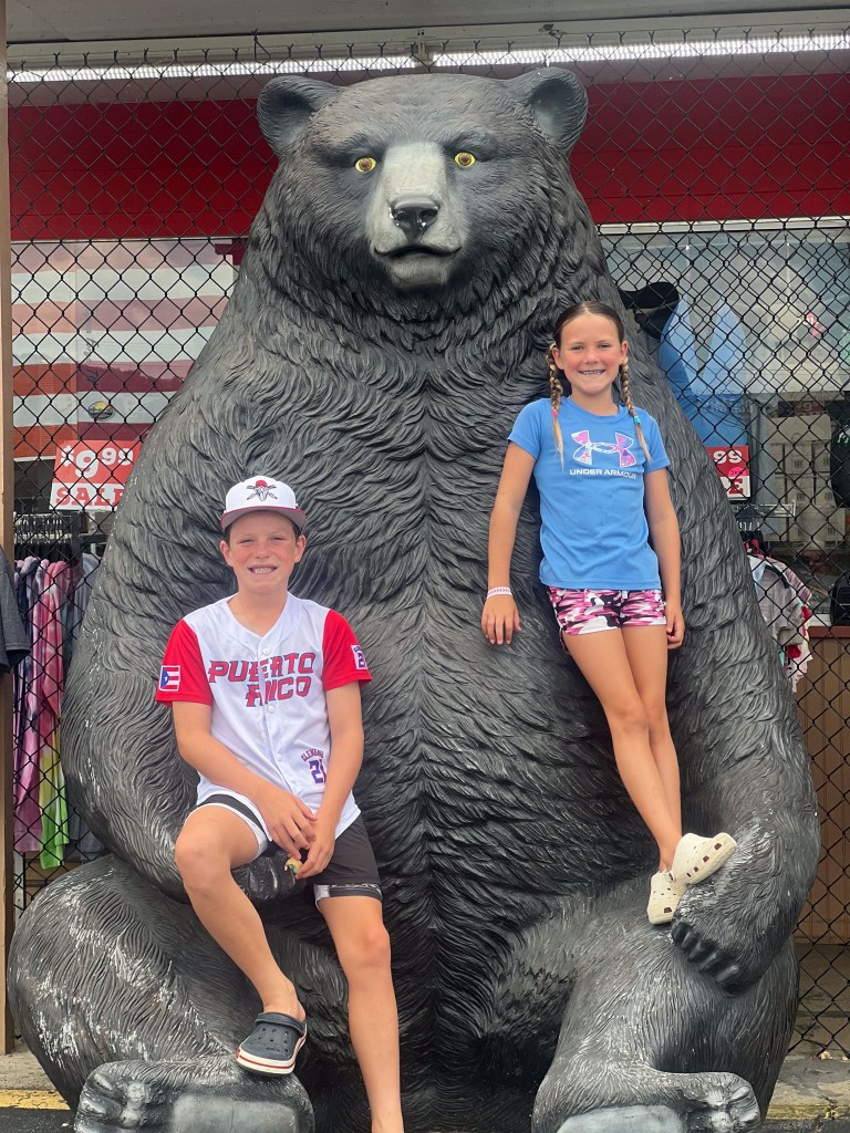 Two children sitting on a large bear statue.