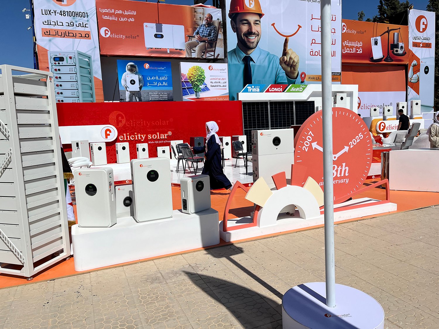 A woman in a white headscarf and long black dress walks through a booth with multiple signs advertising solar power.