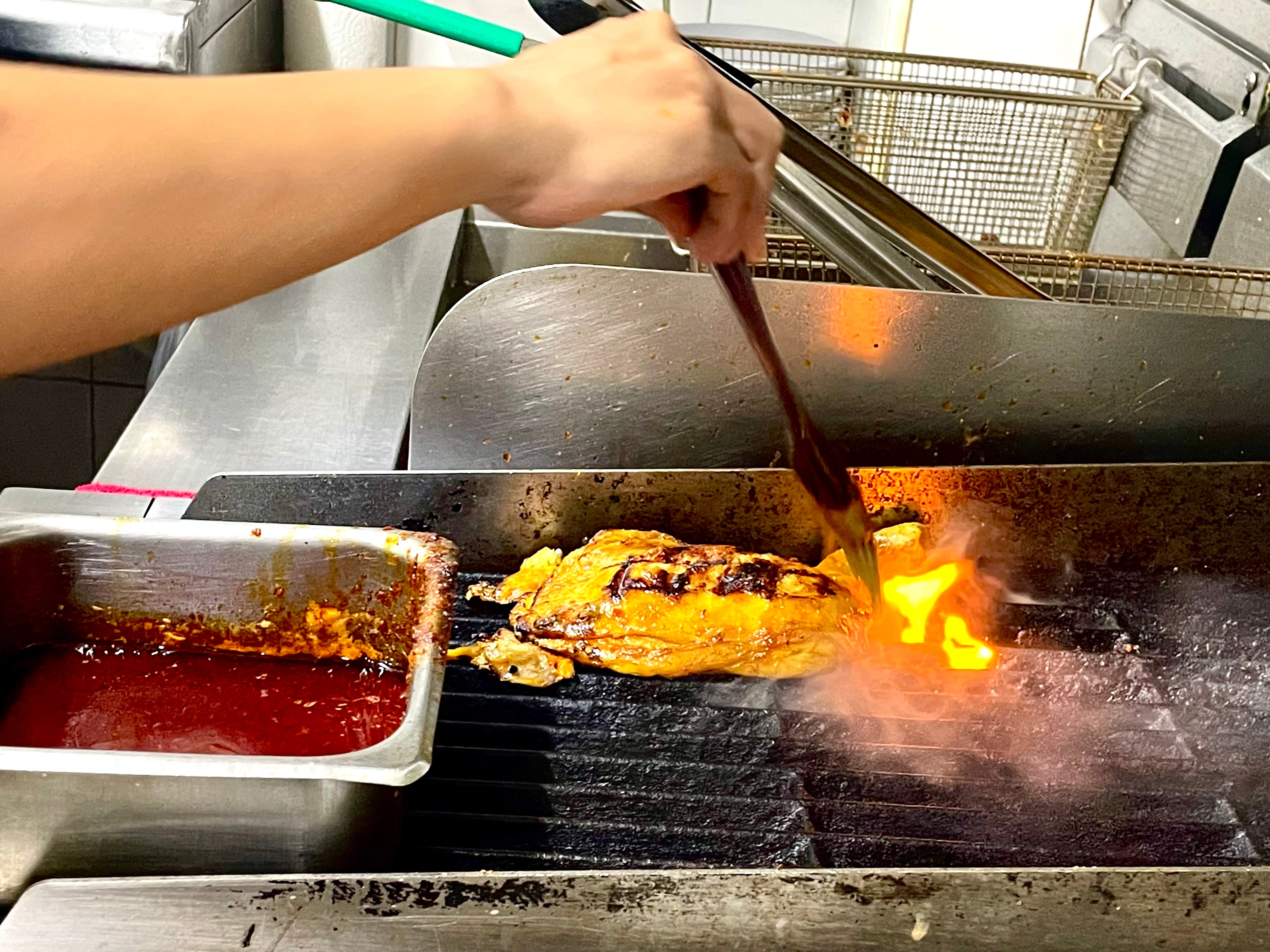A staff member grilling a piece of chicken leg.