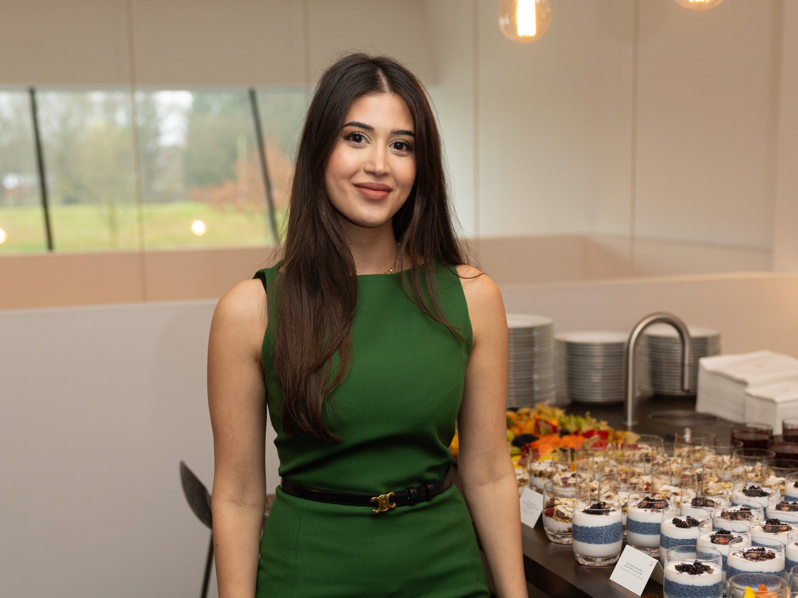 A woman in a green dress stands next to a table of carefully prepared breakfast portions