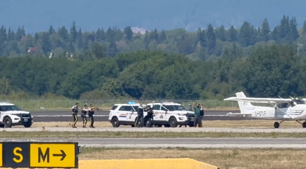 Police officers apprehending a suspect on an airport tarmac near a small plane.