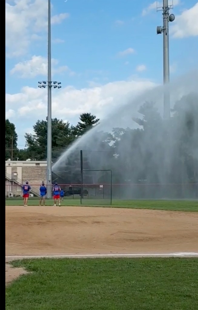 Firefighter spraying a baseball field with a hose.