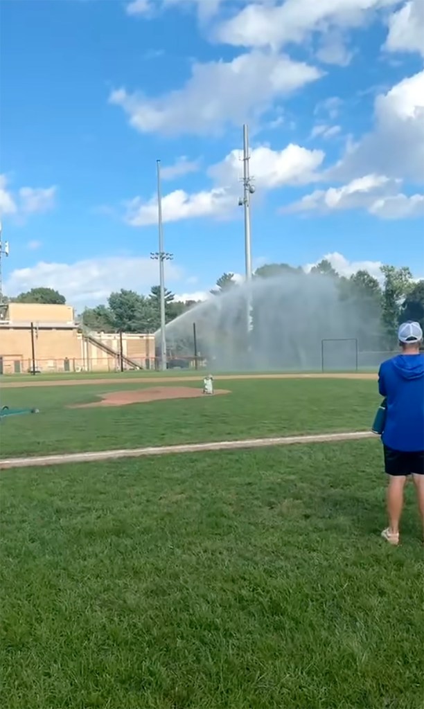 Firefighter spraying a baseball field with a firehose.