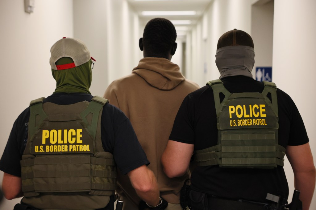 A man in custody escorted by two U.S. Border Patrol agents.