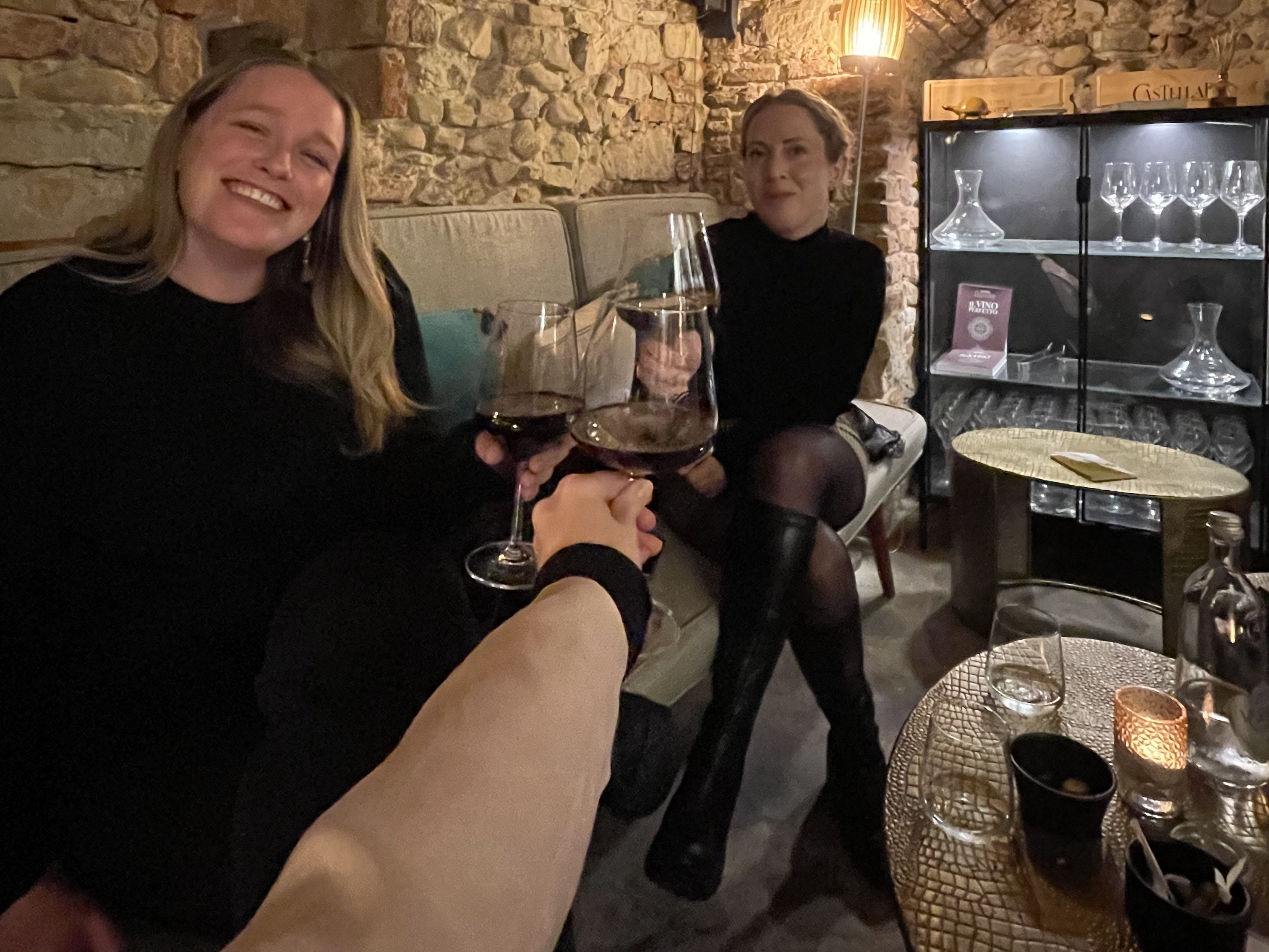two young women sit in wine cellar with filled wine glasses in hand