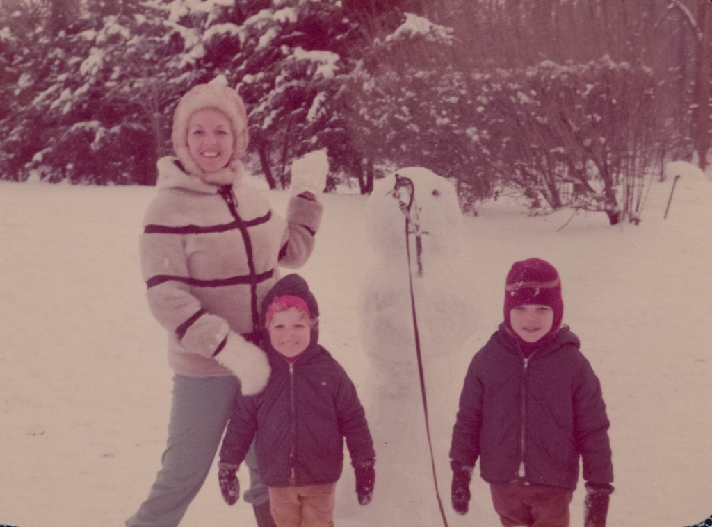 Woman and two children playing in the snow near a snowman.