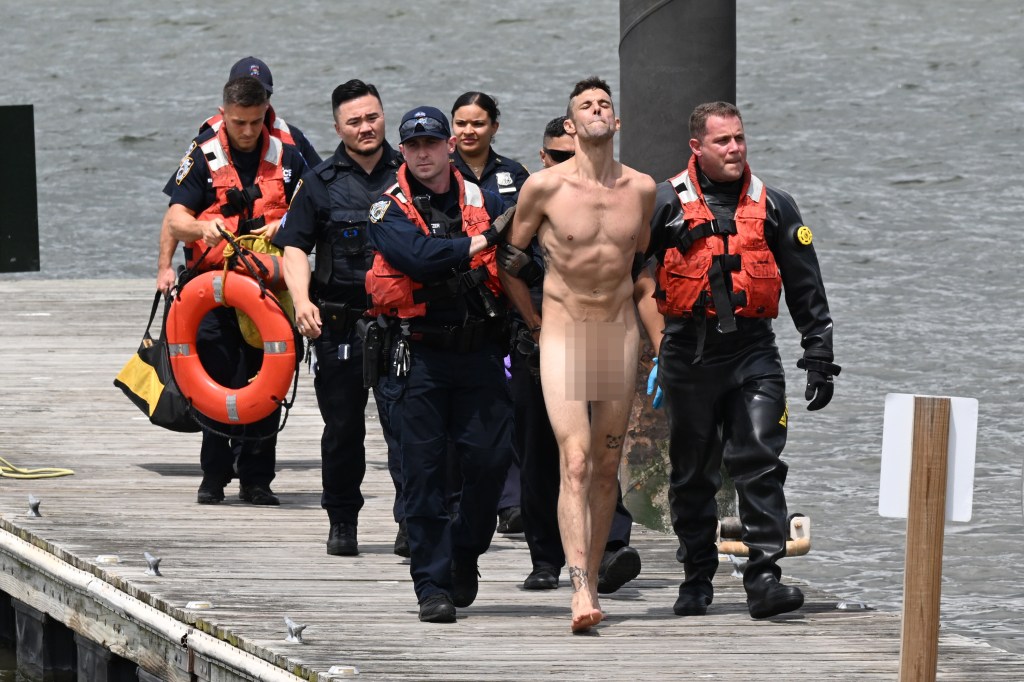 A naked man in police custody walks on a dock.