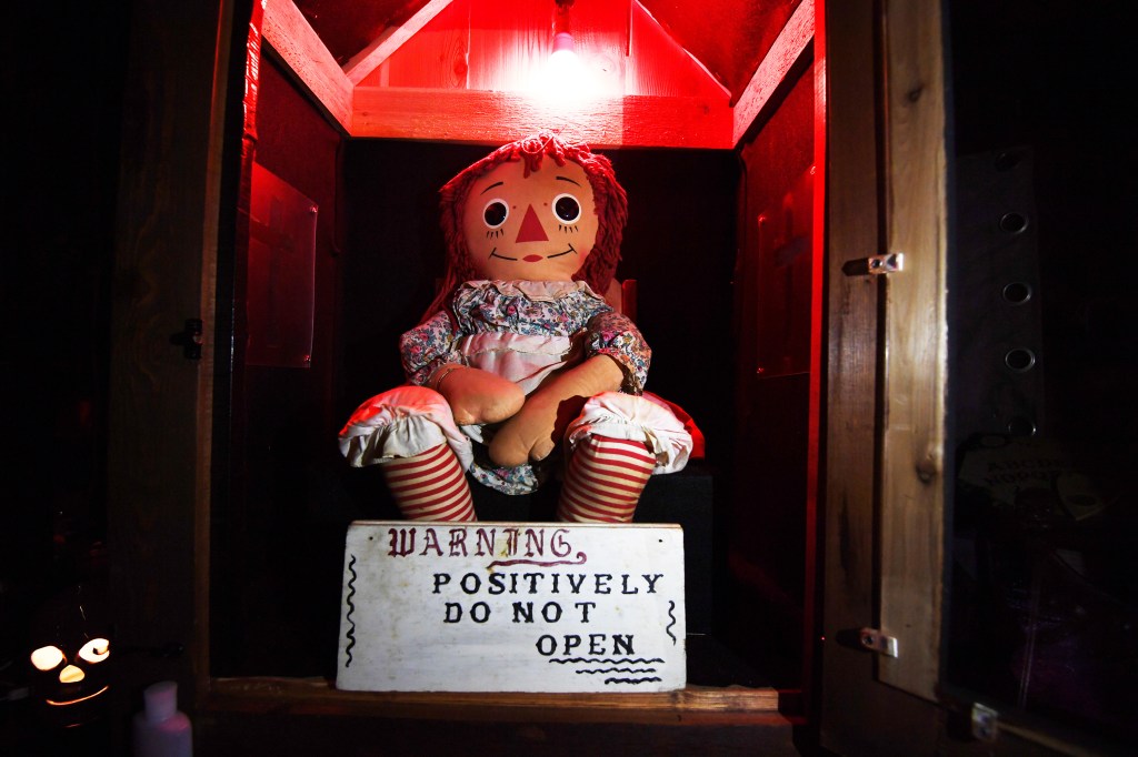 Annabelle doll in a glass case with a warning sign.