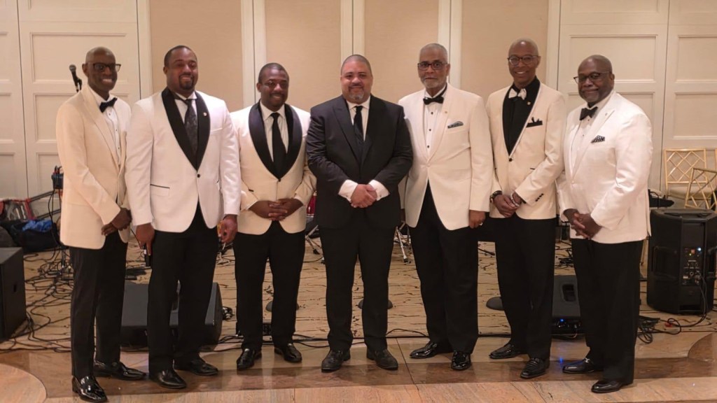Group photo of seven men -- including Bragg -- in formal wear.