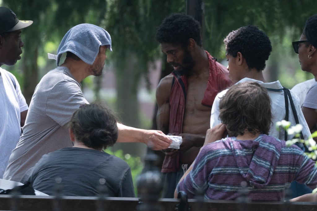 A man handing something to a group of people in a park.