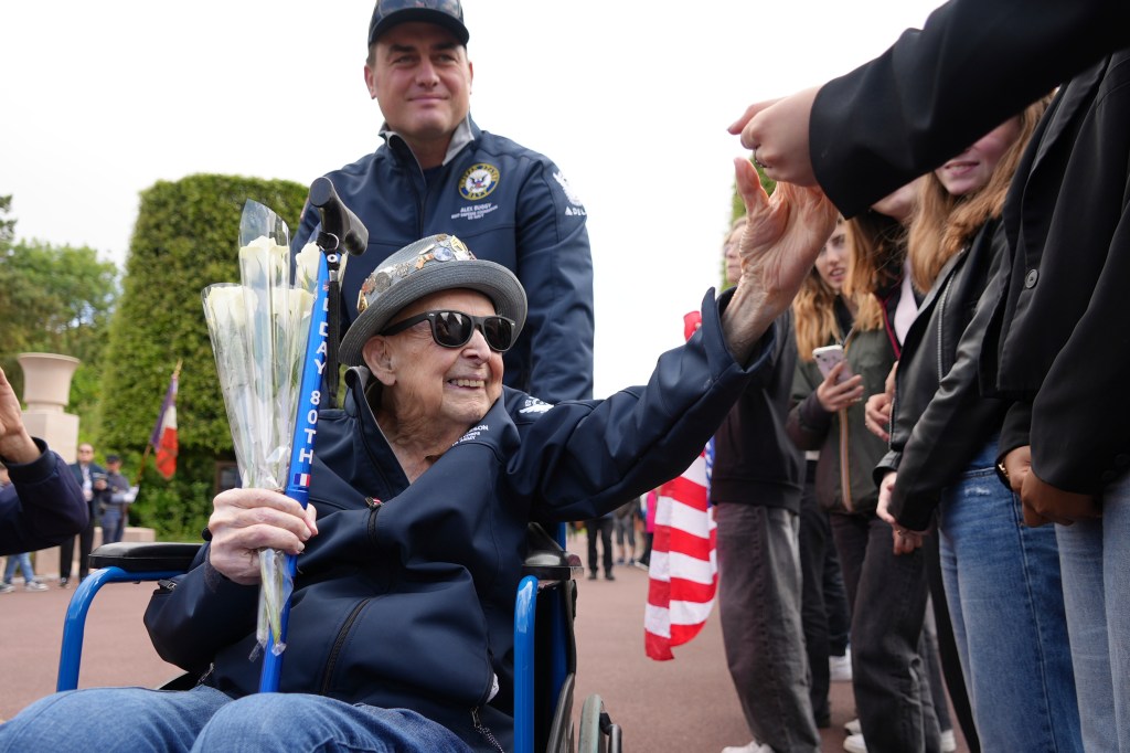 A 102-year-old D-Day veteran in a wheelchair high-fives schoolchildren.