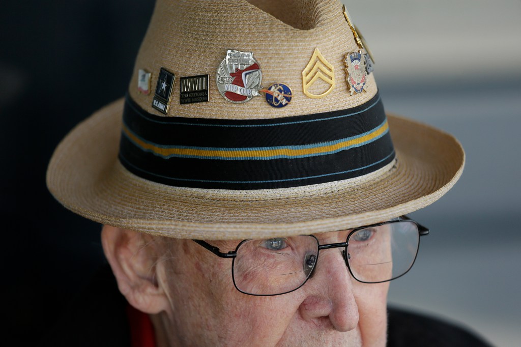 Close-up of a man wearing a straw hat adorned with military pins.