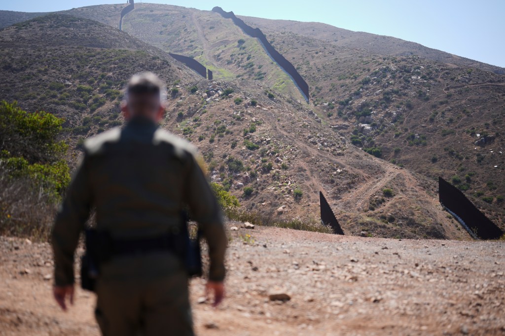 Border Patrol agent walking toward a border wall.