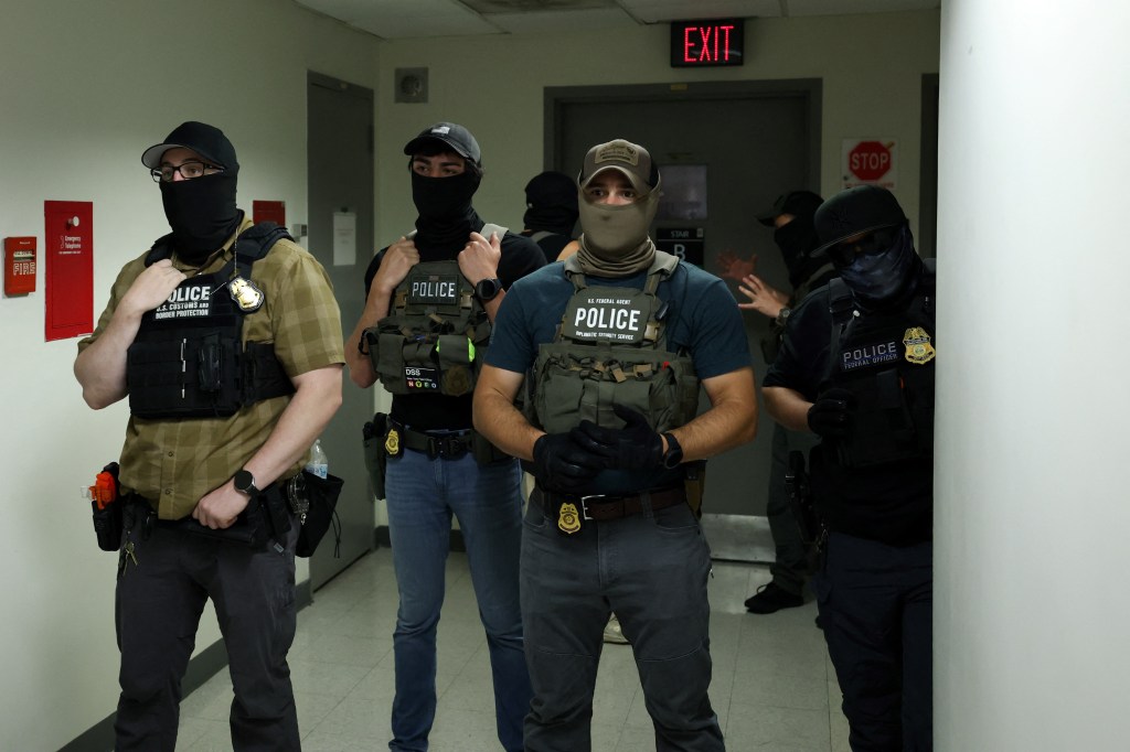 Federal officers in tactical gear wait in a hallway.