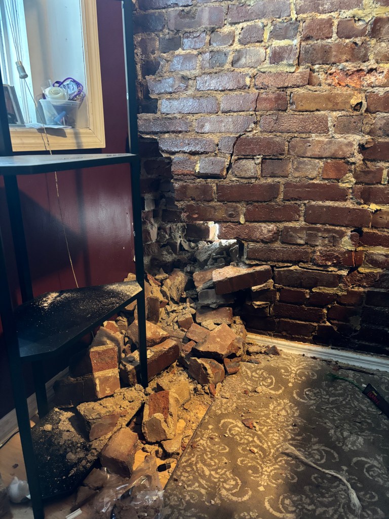 A hole in a brick wall, with rubble on the floor.