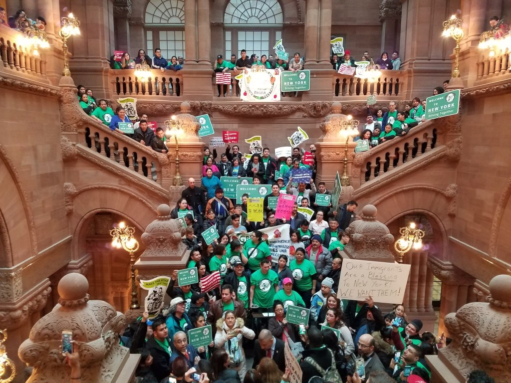 Large group of people holding signs at a rally in a grand building's staircase.