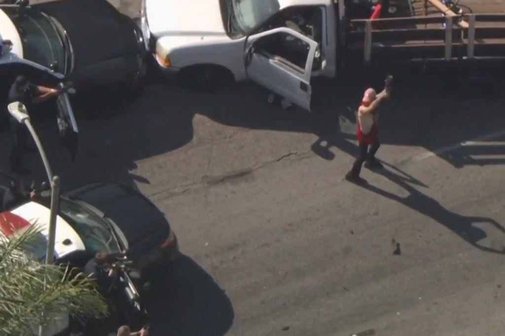 Person standing in street near several damaged vehicles and police officers.