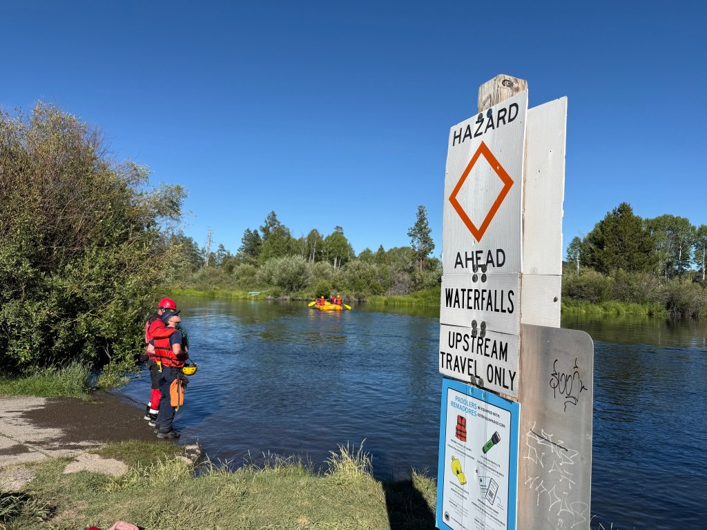 Rescuers at a river near a waterfall hazard sign.