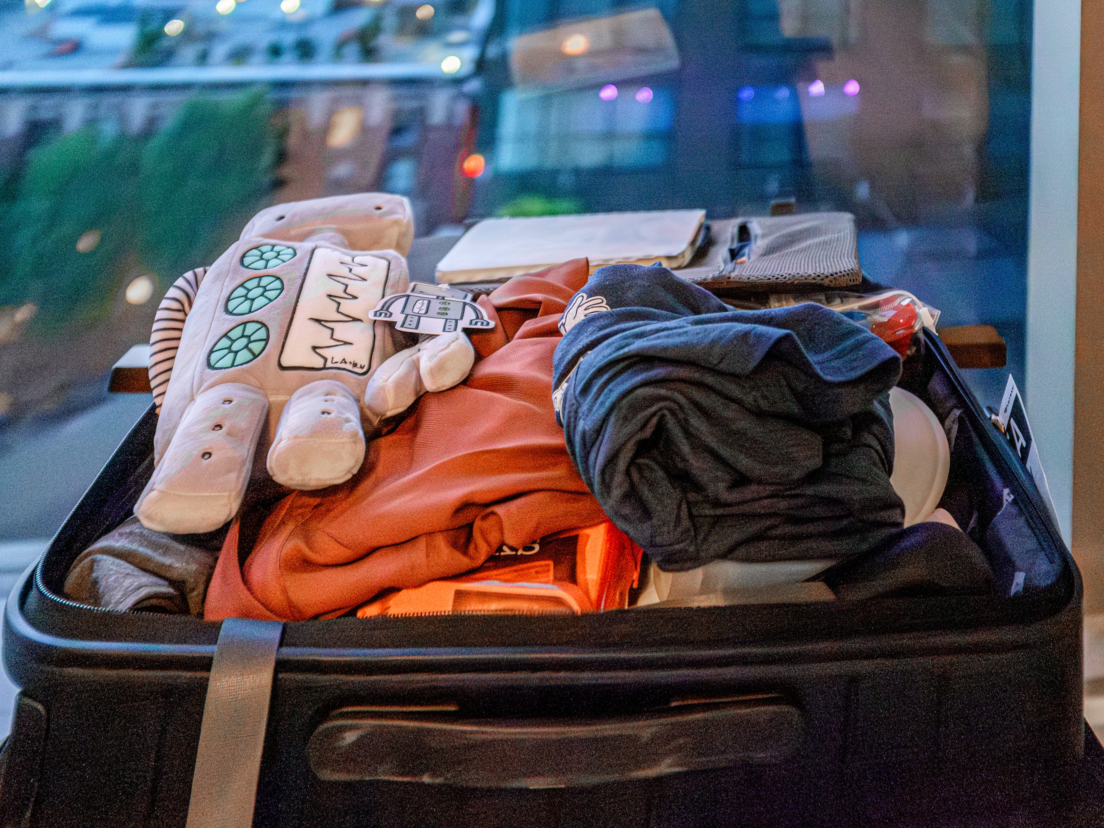 An open suitcase with clothes and a robot plushie on top