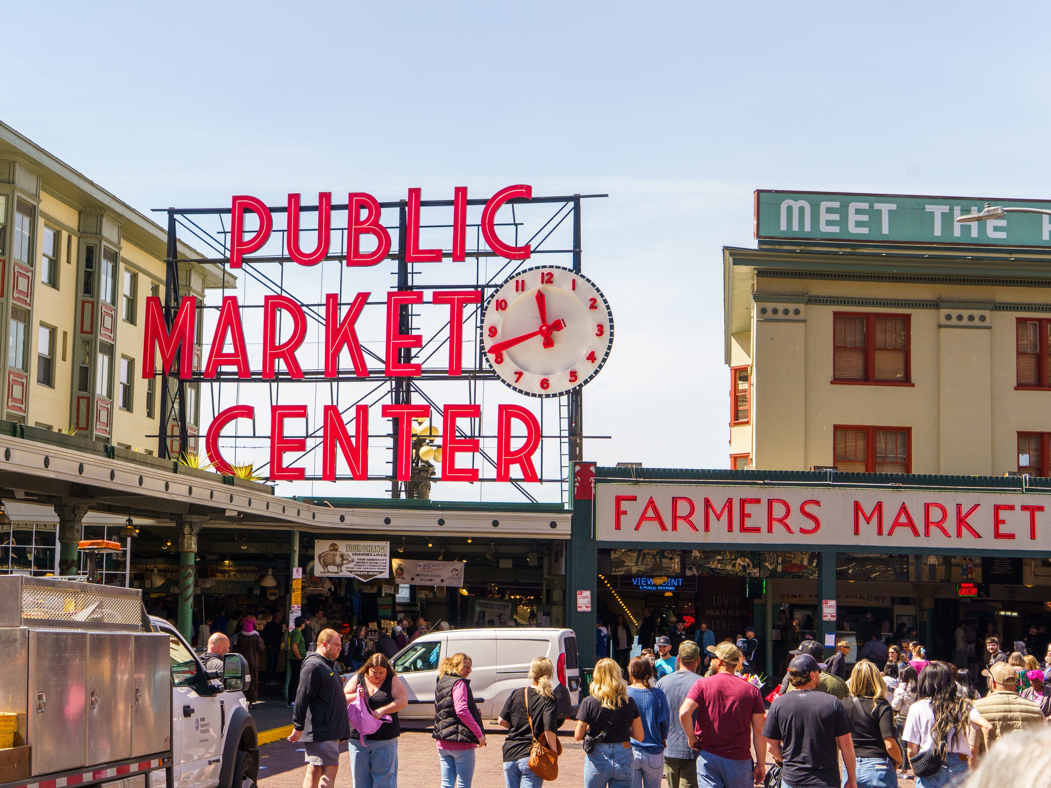 Crowds wander Pike Place Market in Seattle with a bright, red sign above the shops