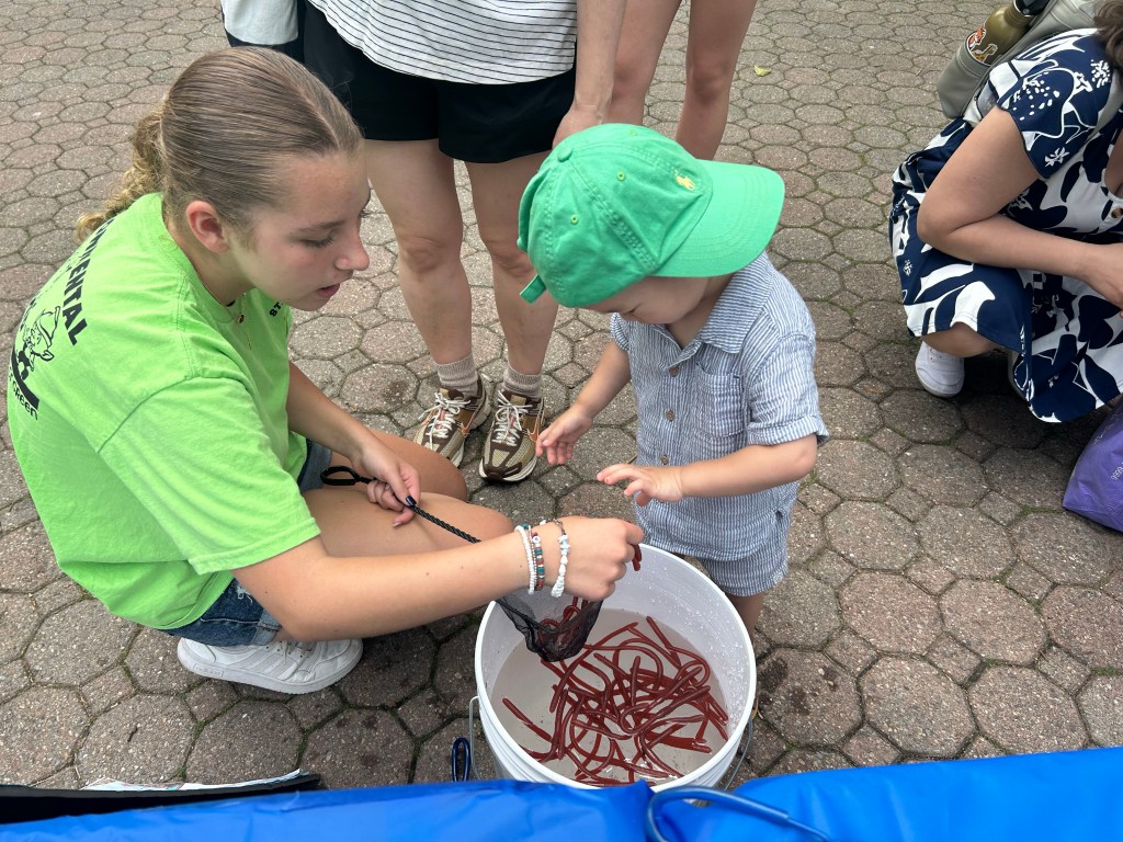 Two kids hold eels in a bucket.