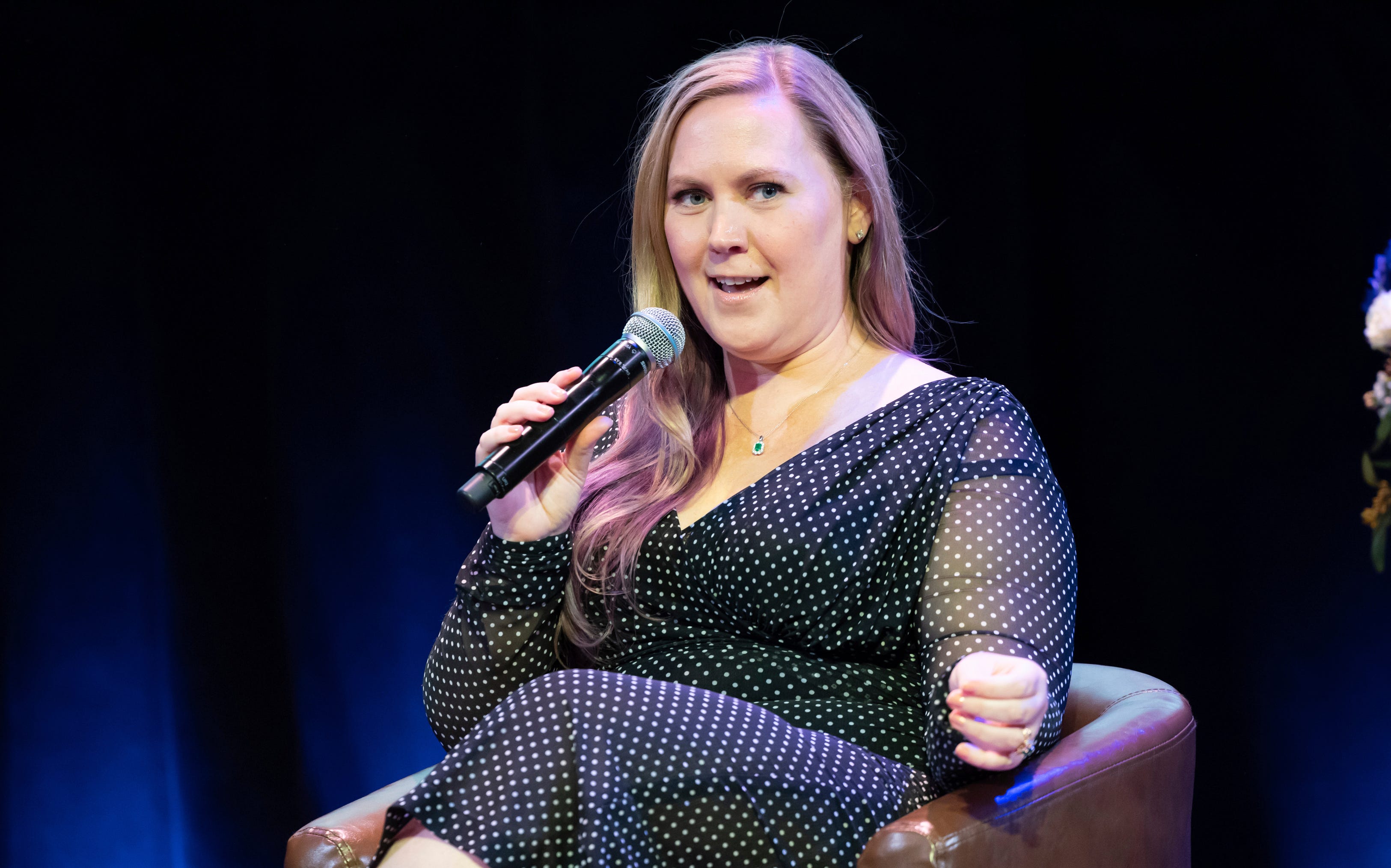 Rebecca Yarros holds a microphone and sits in a chair.