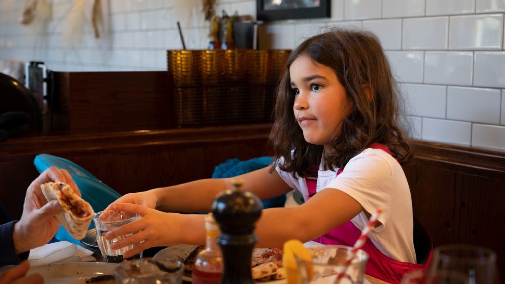 Girl reaching for food at a restaurant table.