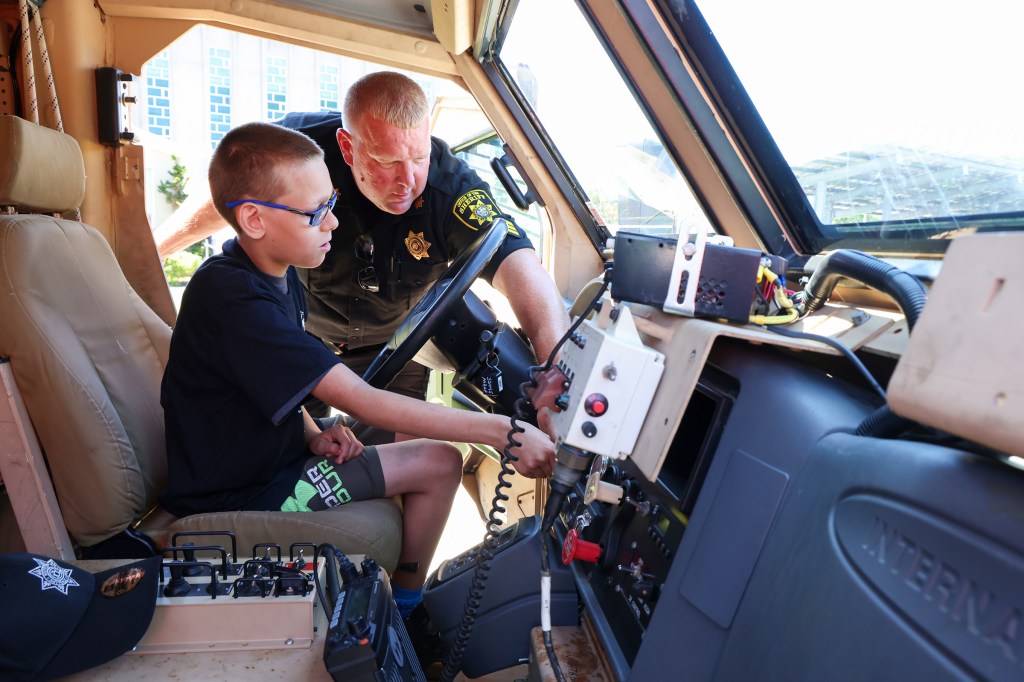 Boy sitting in a sheriff's vehicle with a sheriff.