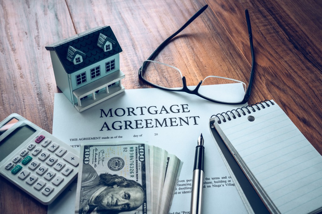 Mortgage agreement with house model, money, calculator, and pen.