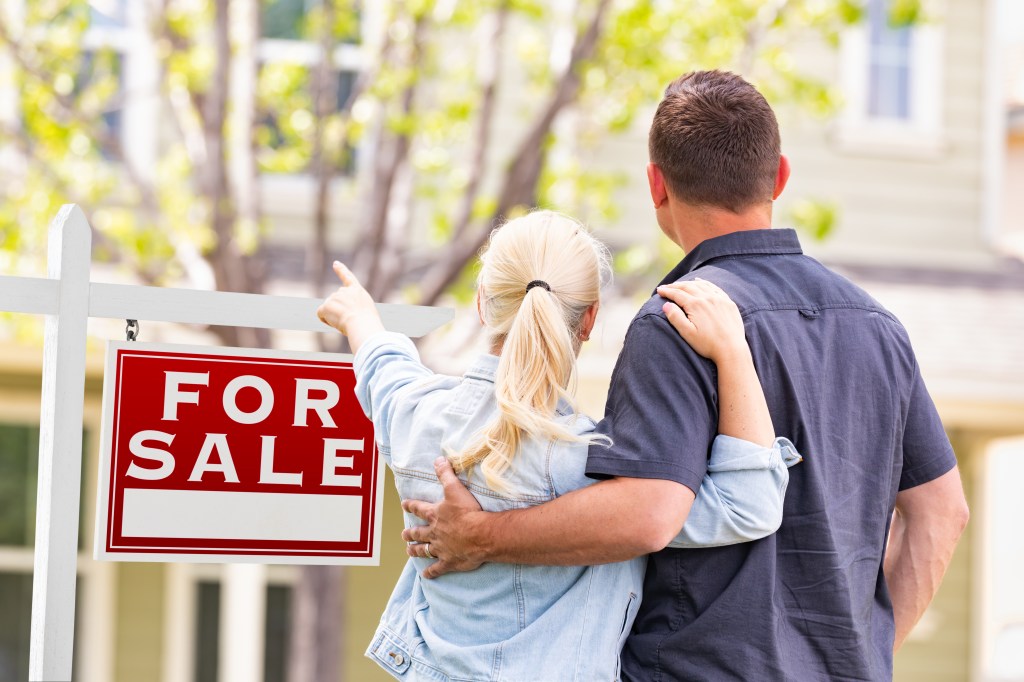 Couple looking at a for sale sign in front of a house.