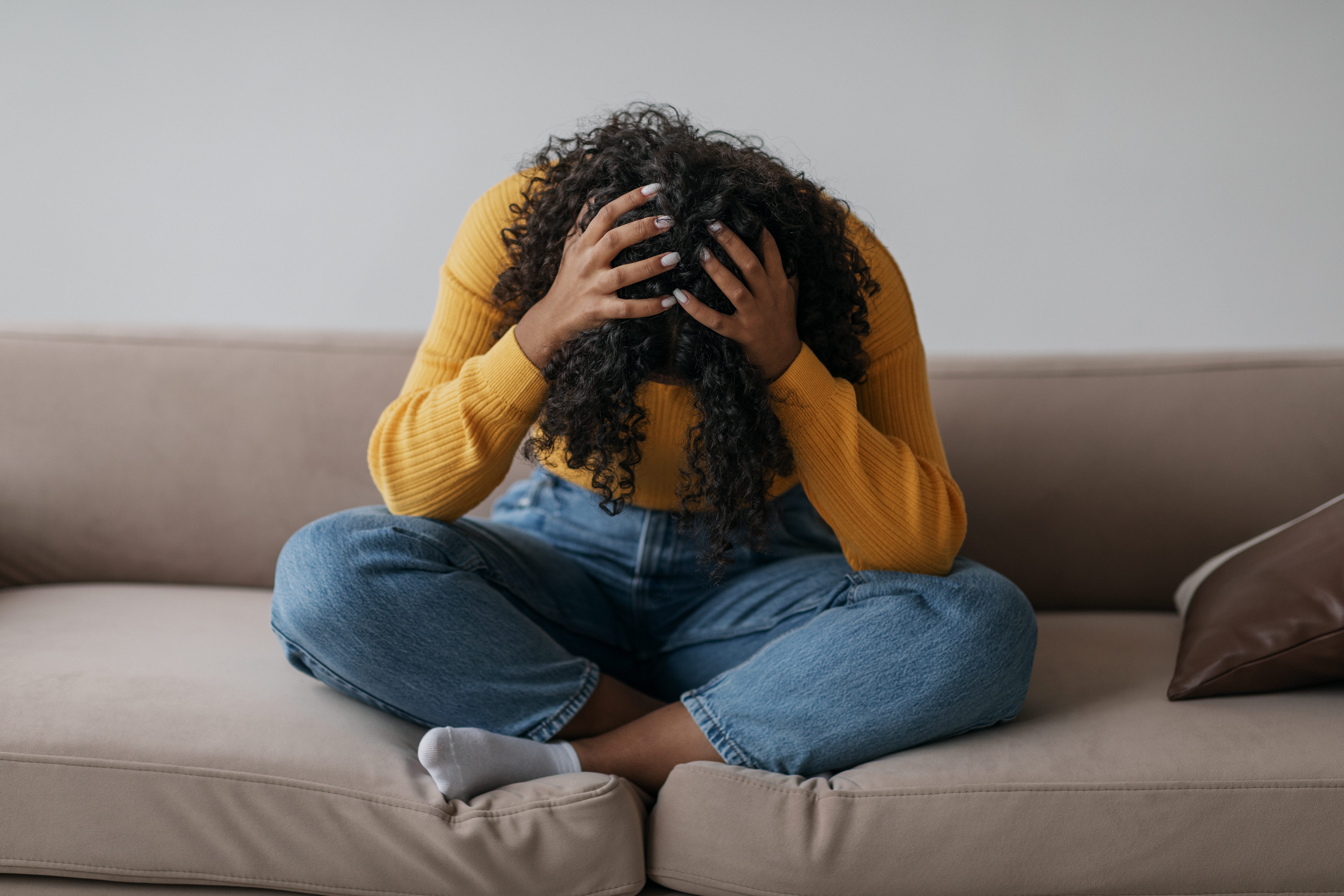 a Black woman sitting on a couch alone looking depressed