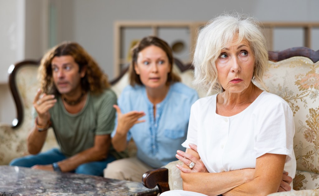 An upset older woman sits apart from a younger couple who appear to be arguing.