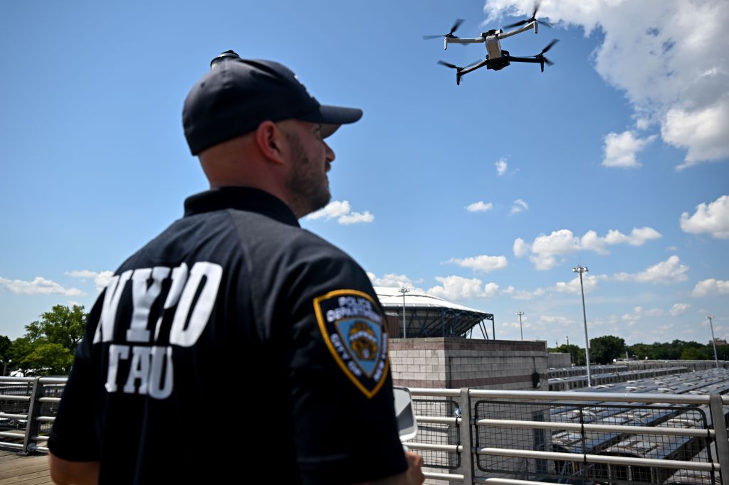 NYPD officer watching a drone fly over subway cars.