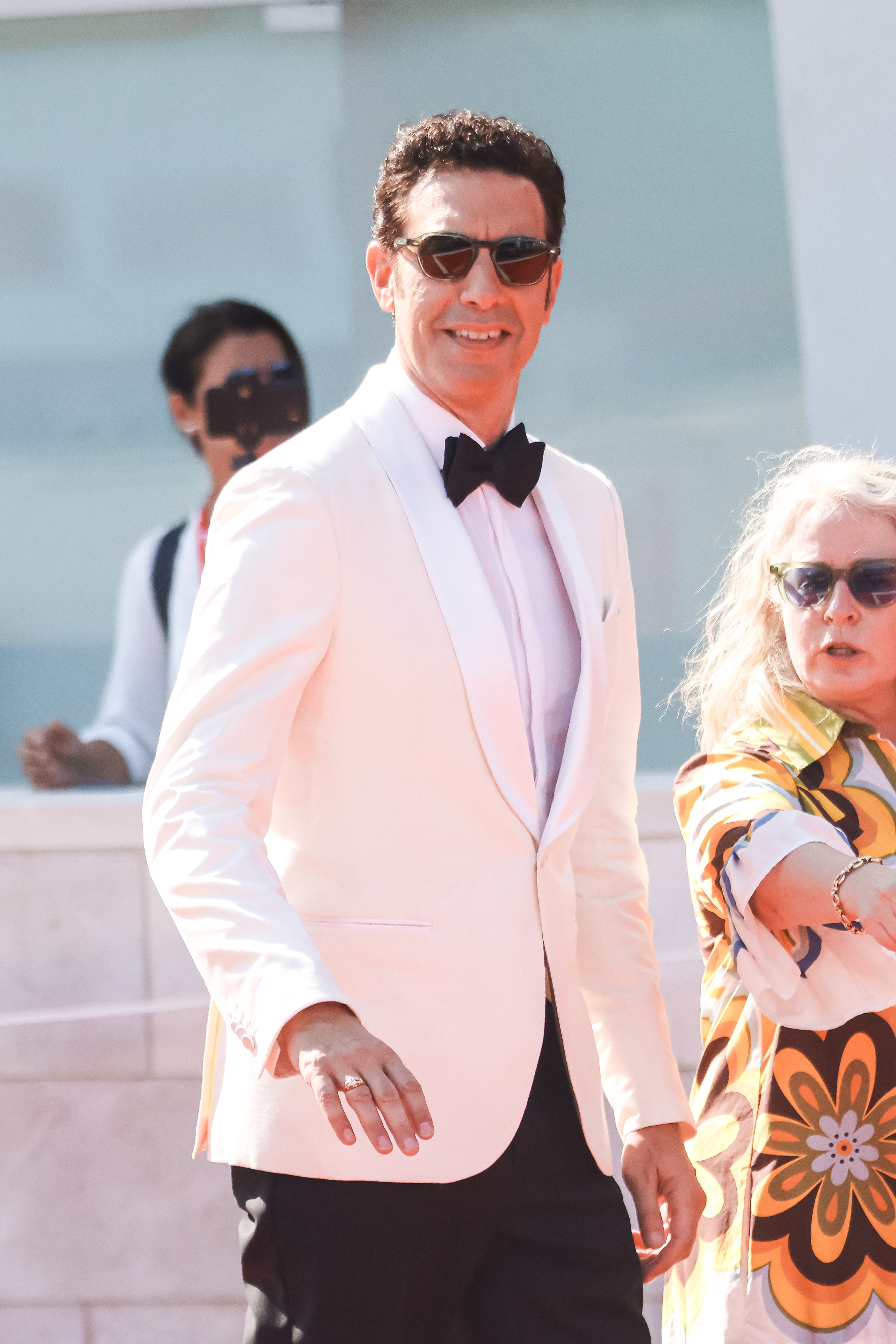 Sacha Baron Cohen in a white tuxedo and sunglasses. 