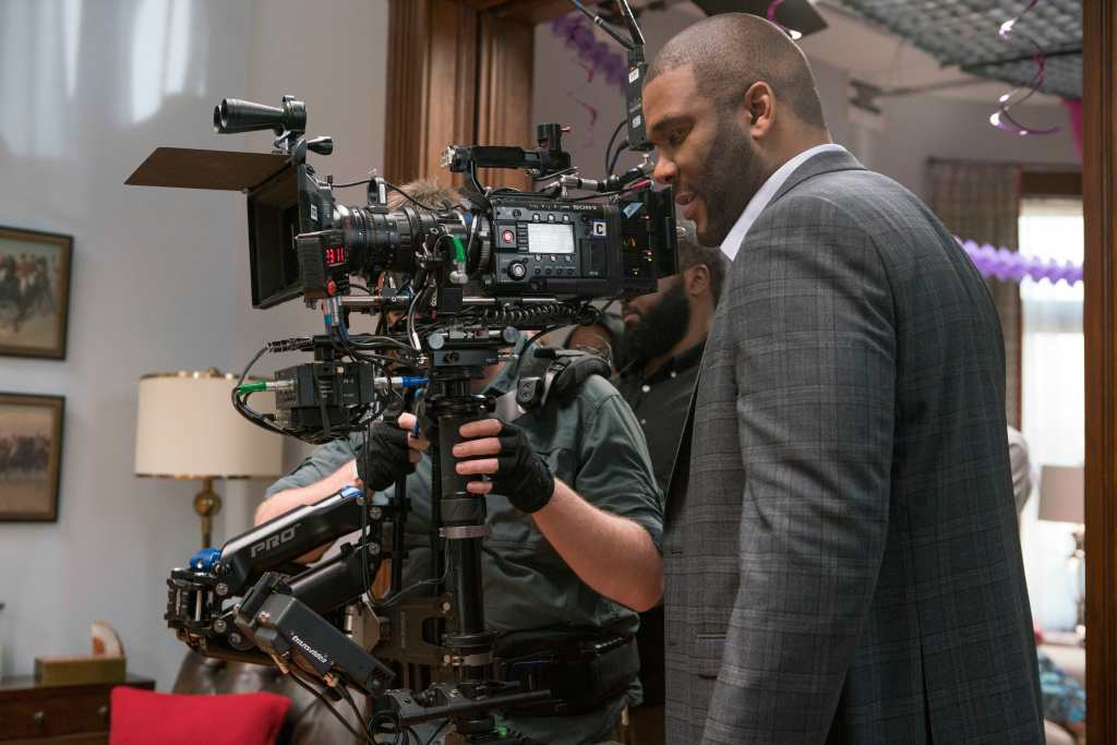 Tyler Perry standing beside a film camera.