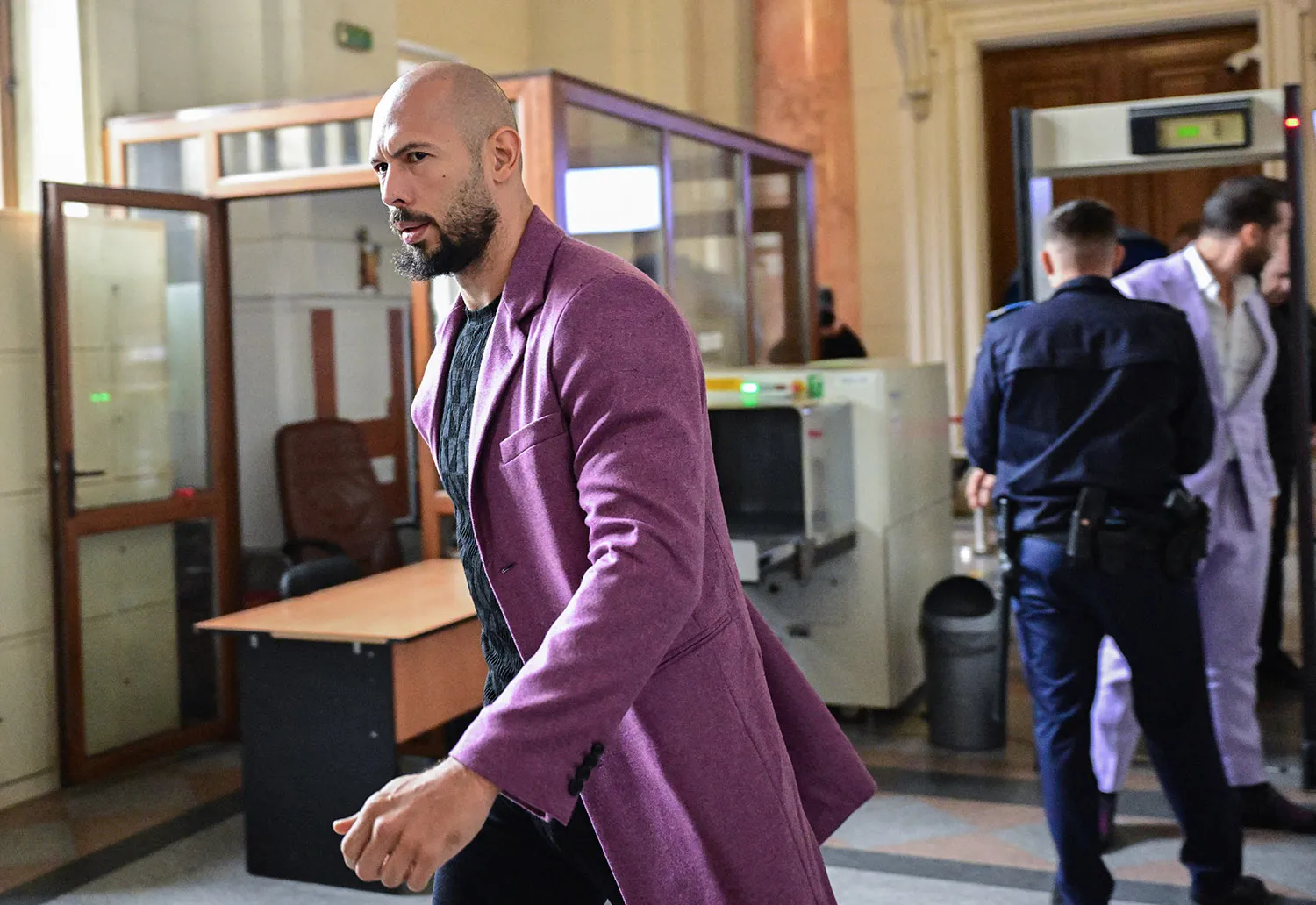 A bald man with a beard in a purple jacket strides through a court building.