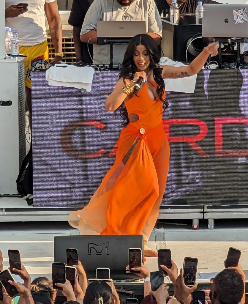 Cardi B stuns in flowing orange swim cover up as she performs her hits 2 hrs late as fans waited in 112 degree heat during fight weekend in Las Vegas.