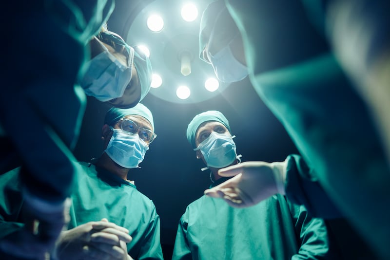 several doctors standing over a patient with a medical lamp above their heads