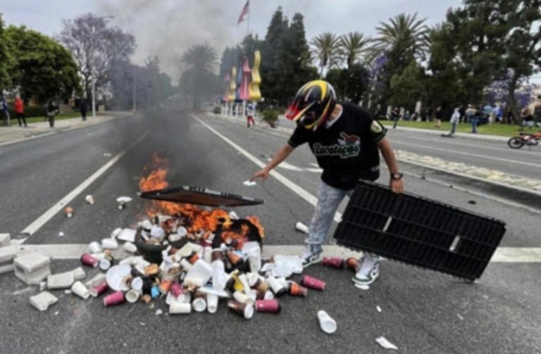 A person in a helmet sets fire to trash in a street.