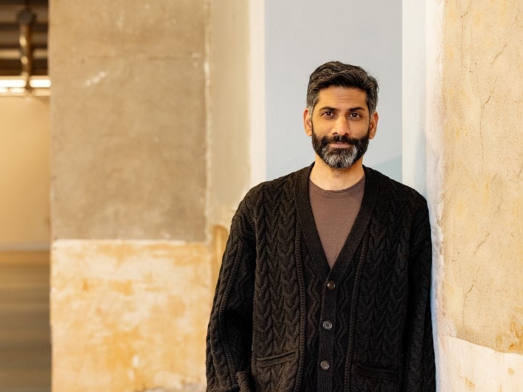 An Indian-American man leans against a concrete wall.