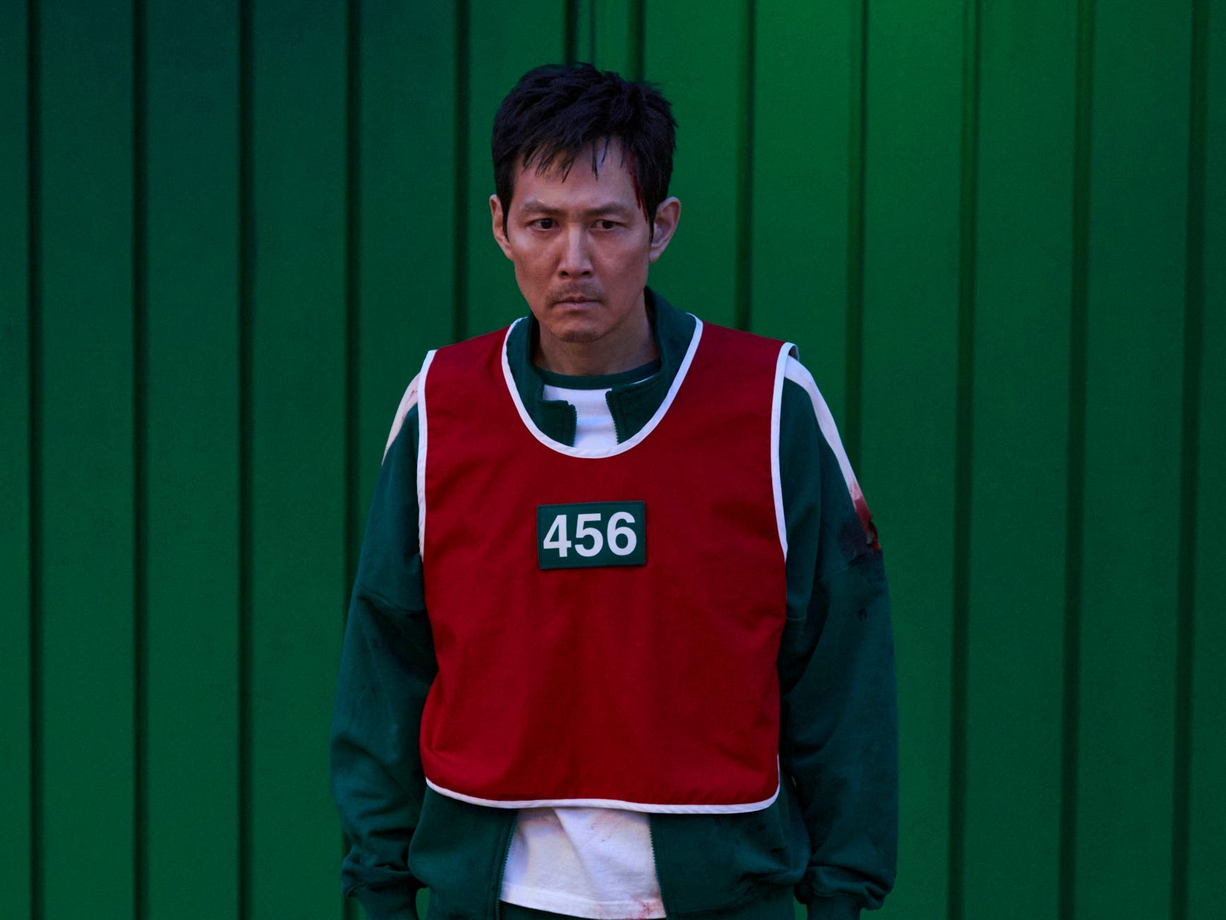 A still of "Squid Game" showing Lee Jung-jae in a bloody green tracksuit and red vest.