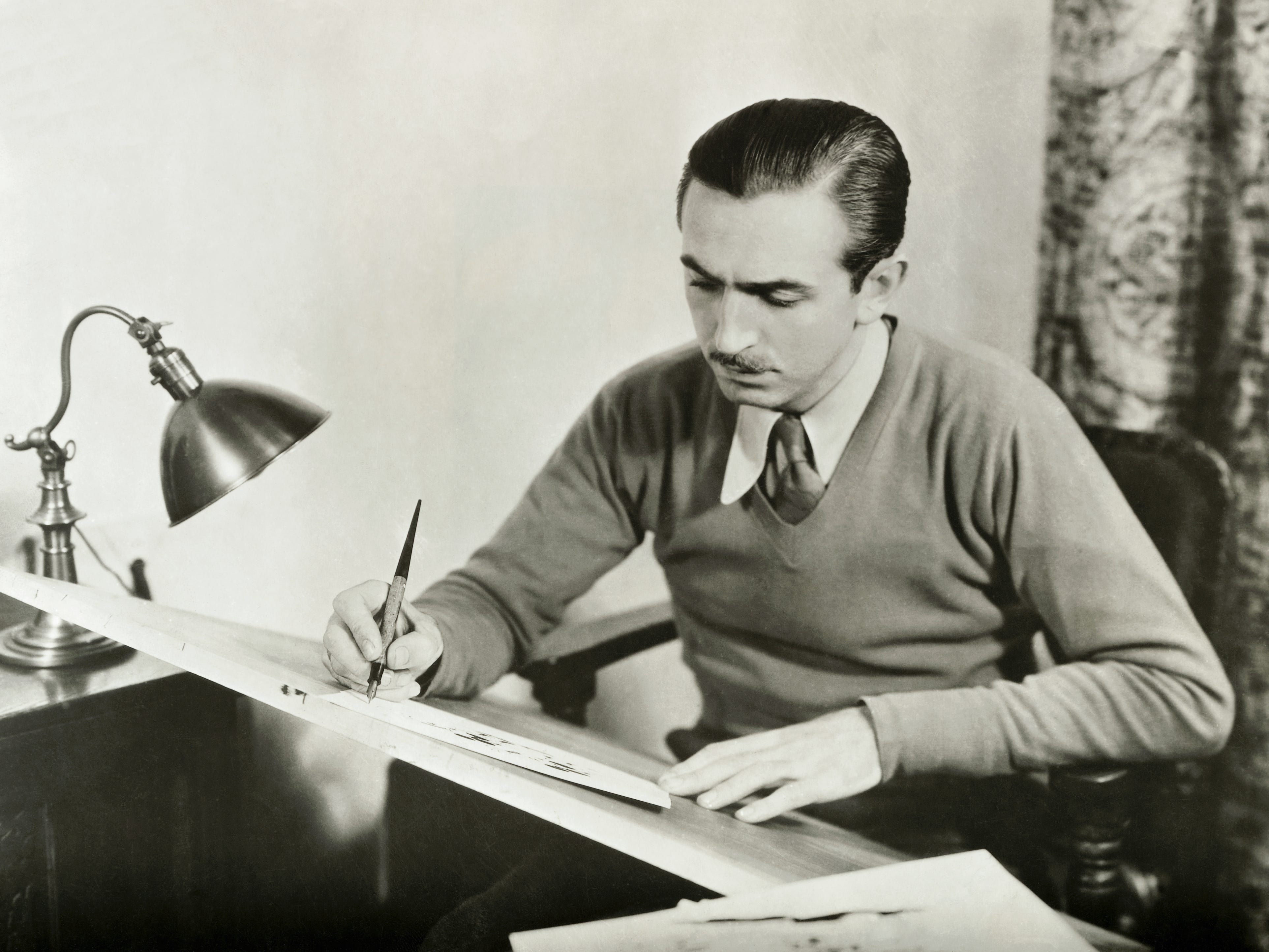 Walt Disney drawing at a slanted desk.