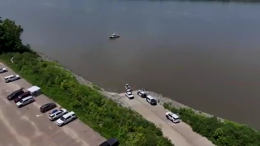 Aerial view of a riverbank with emergency vehicles and a boat.