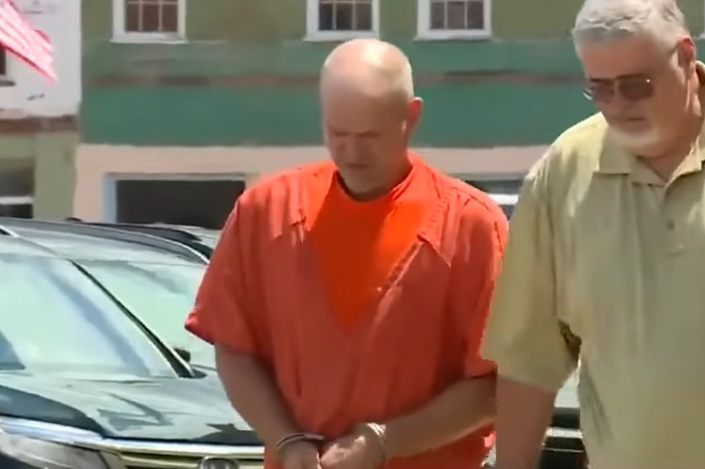 A handcuffed man in an orange jumpsuit walks alongside another man.