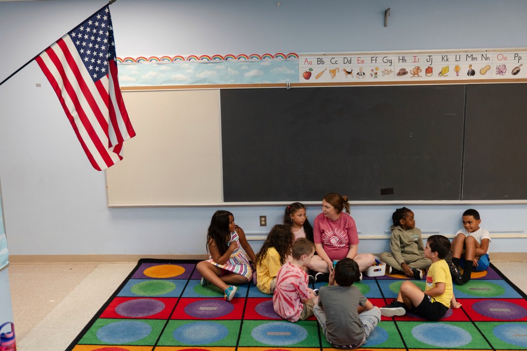 Children sitting on a colorful rug in a classroom with a teacher.