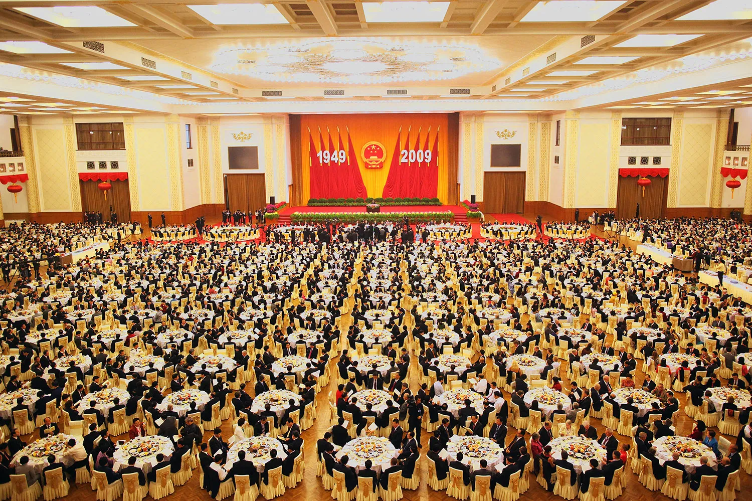 A large formal hall filled with people around hundreds of circular tables.