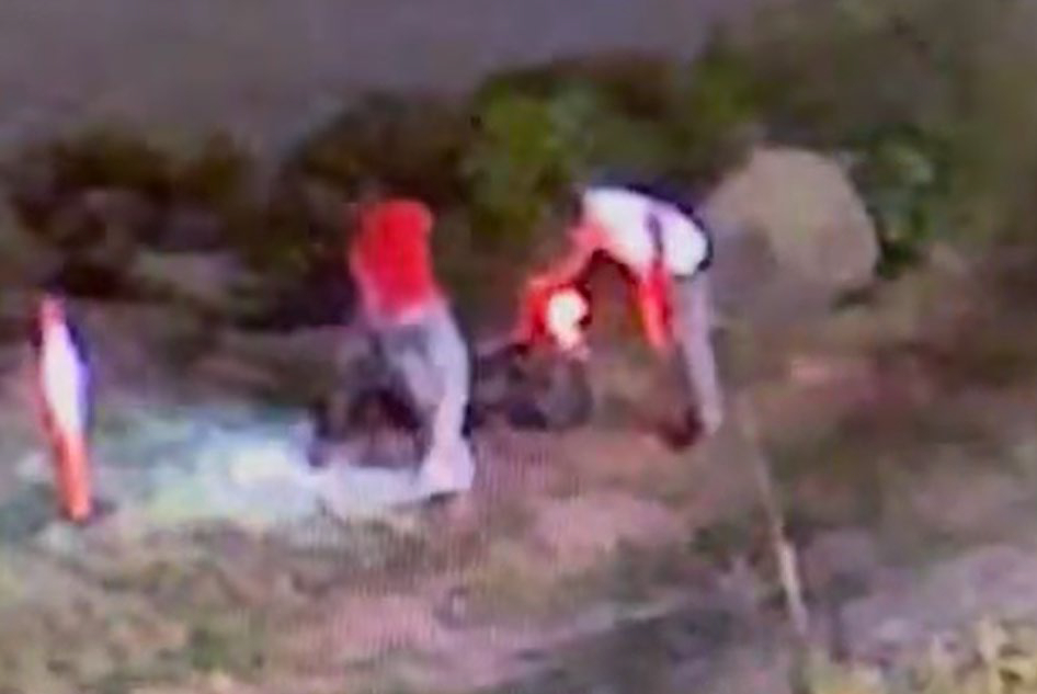Low-quality surveillance footage of two people tending to a person on the ground.
