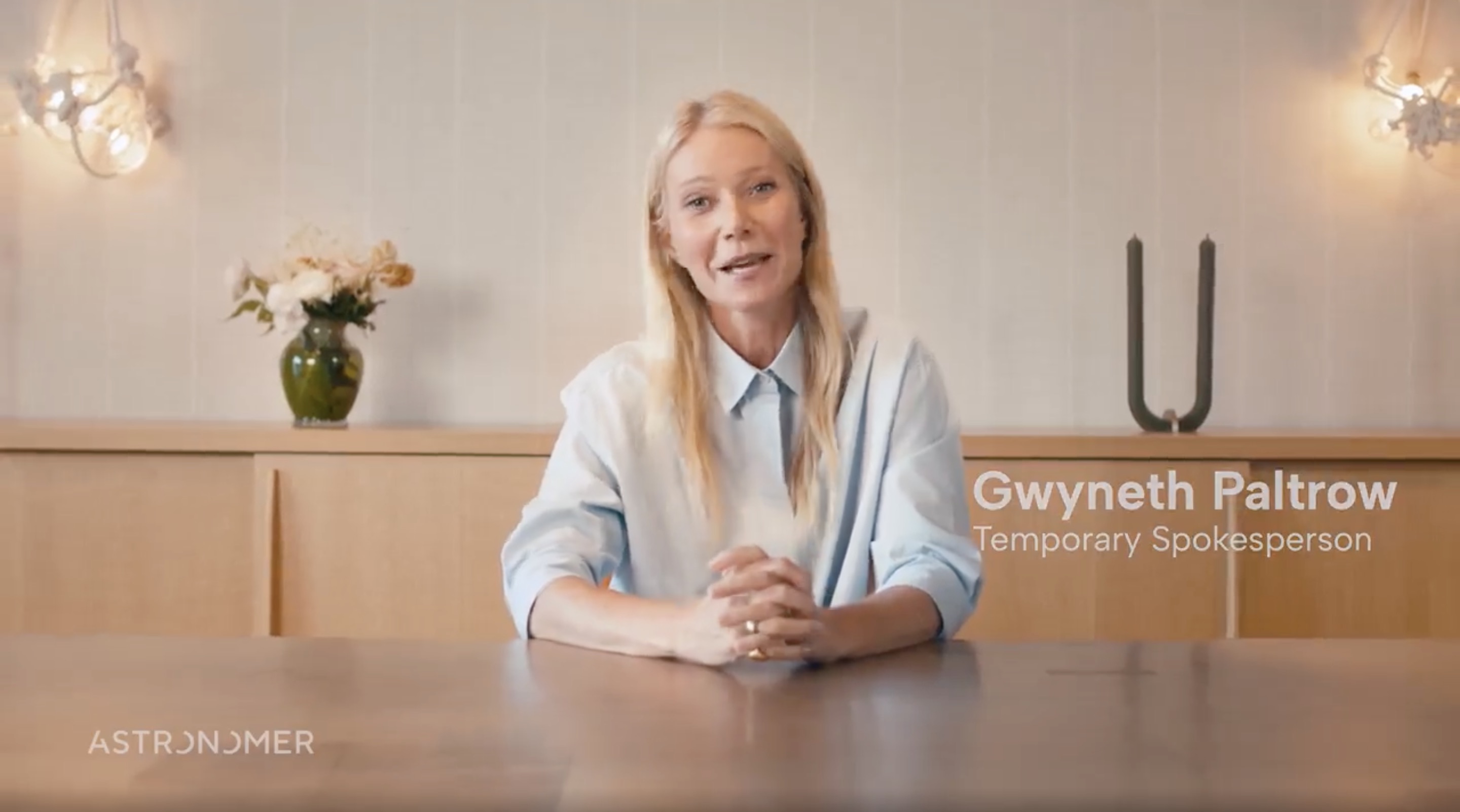 Gwyneth Paltrow sits at a desk and smiles. 
