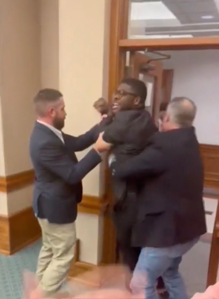 A congressional candidate being forcibly removed from a hearing.