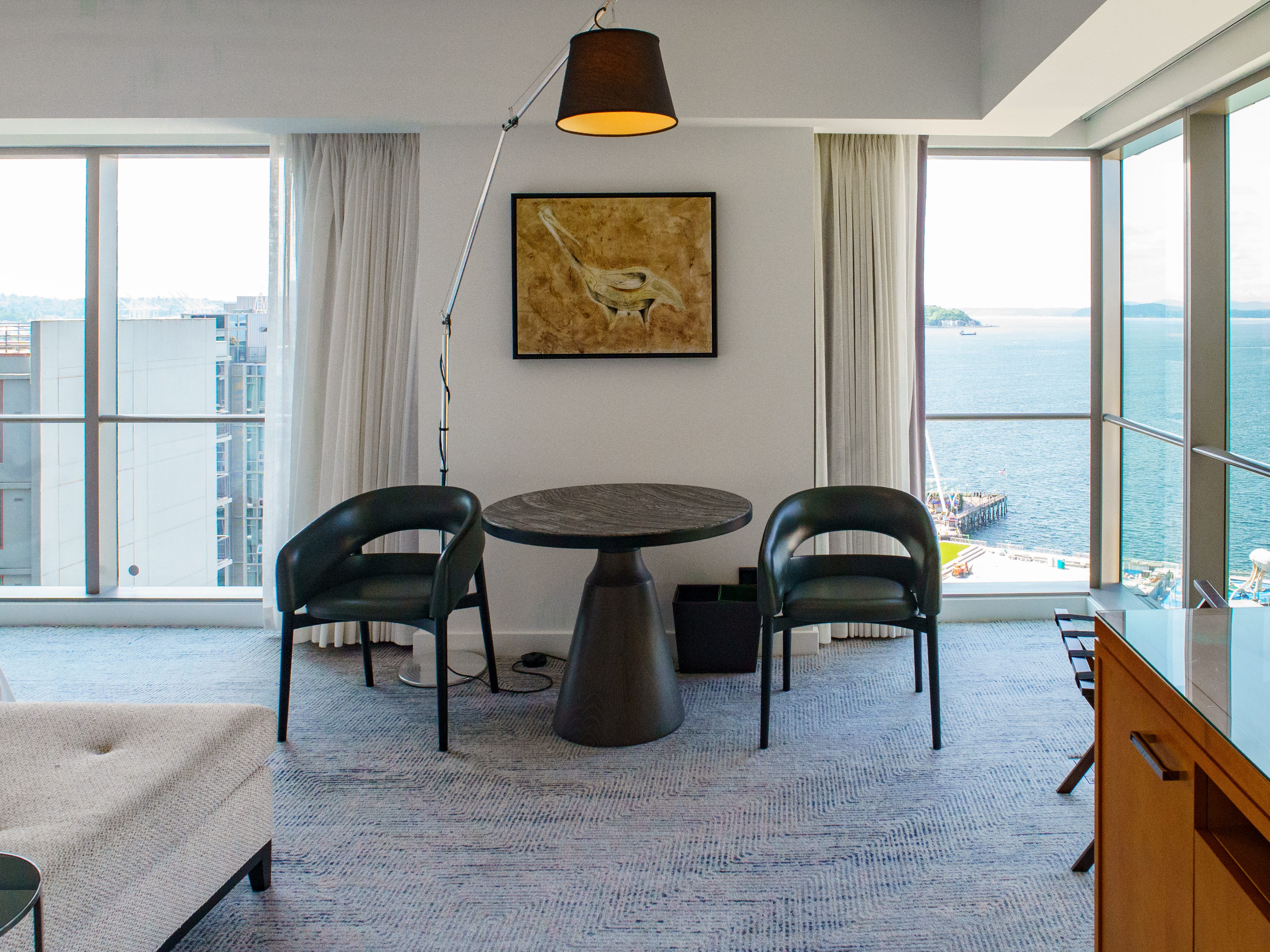Inside a Four Seasons Seattle hotel room with floor-to-ceiling windows and a lamp hanging over a table and chairs